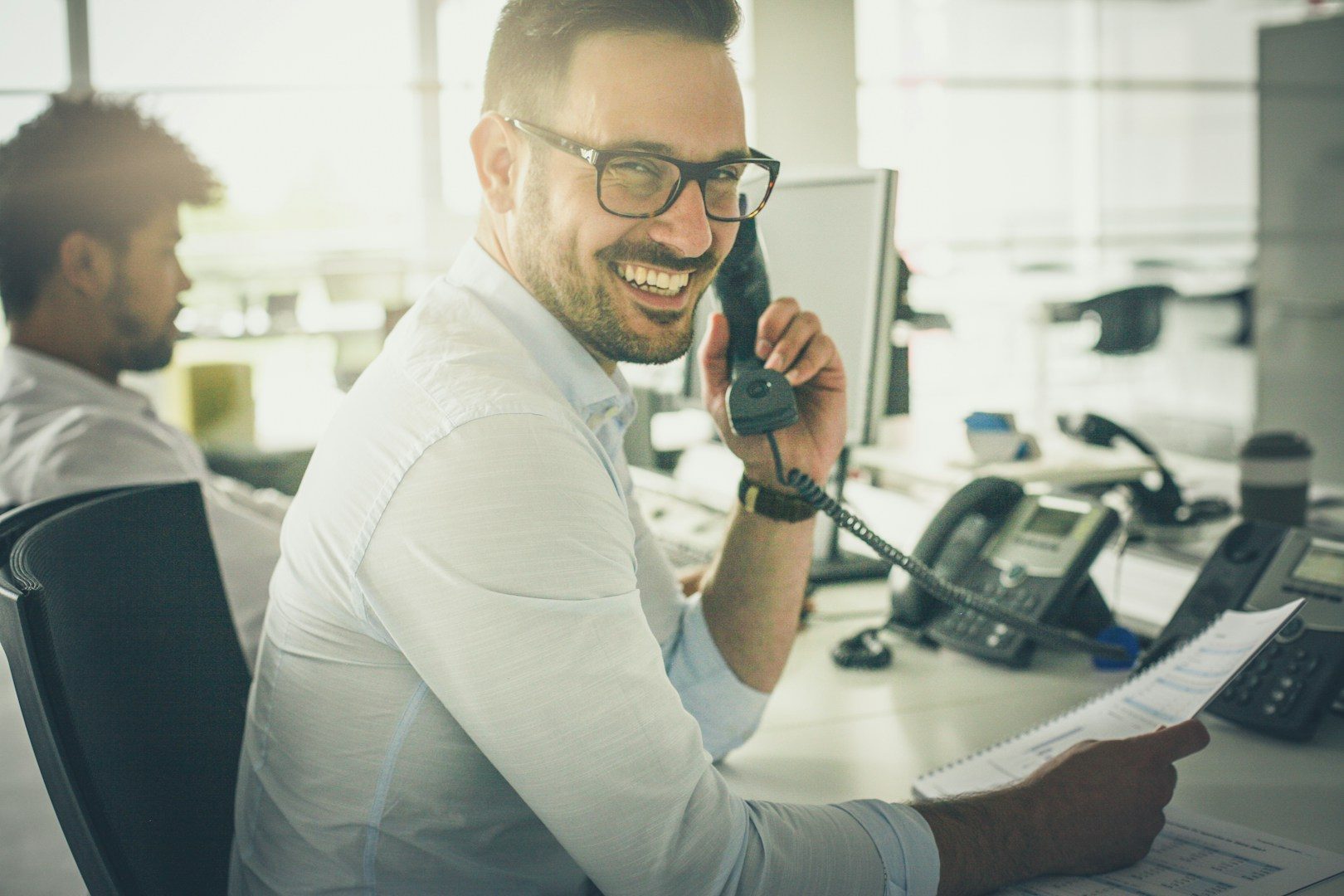 Mann am Telefon mit Brille, lächelnd, in einem modernen Büro.