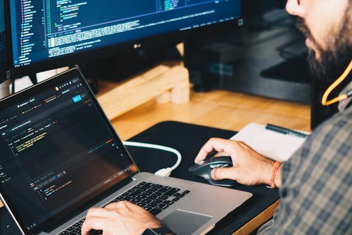 Ein Mensch arbeitet an einem Laptop mit offenem Code und nutzt eine Maus.
